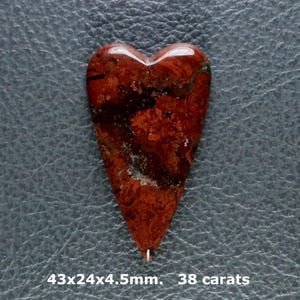 May include: A heart-shaped stone pendant featuring a mottled pattern of deep red, brown, and black colors. The stone is labeled with dimensions of 43x24x4.5mm and a weight of 38 carats. The surface has a polished finish with visible natural inclusions.
