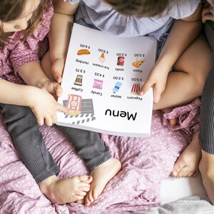 May include: A white menu with black text and images of food items. The menu lists prices for popcorn, water, candy, coffee, pizza, soda, ice cream, and hotdogs. Two children are looking at the menu.