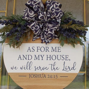 May include: A round wooden sign with the text "AS FOR ME AND MY HOUSE, we will serve the Lord - JOSHUA 24:15". The sign is decorated with a navy blue and white patterned bow and greenery.