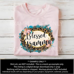 Puede incluir: Una camiseta rosa con un dise&ntilde;o que presenta un fondo de estampado de leopardo, salpicaduras de pintura azul turquesa y flores rosas. El dise&ntilde;o tambi&eacute;n incluye un &oacute;valo dorado con el texto "Blessed Gramma".