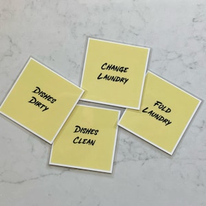 May include: Four yellow sticky notes with black handwritten text. The notes say "Dishes Dirty", "Dishes Clean", "Change Laundry", and "Fold Laundry".