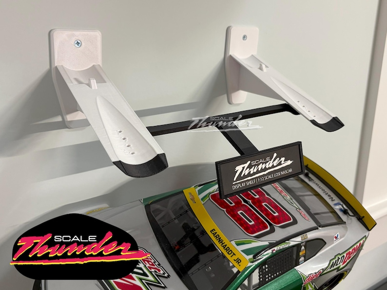 May include: White and black display shelf for a 1:12 scale NASCAR model car. The shelf is mounted on a wall and features the "Scale Thunder" logo. The model car has the number 88 and the name "Earnhardt Jr."