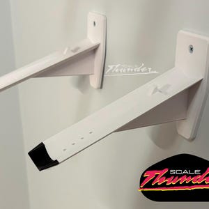May include: Two white wall-mounted shelf brackets with black end caps. The brackets are angled and attached to the wall with screws. The logo "SCALE Thunder" is in the bottom right corner.