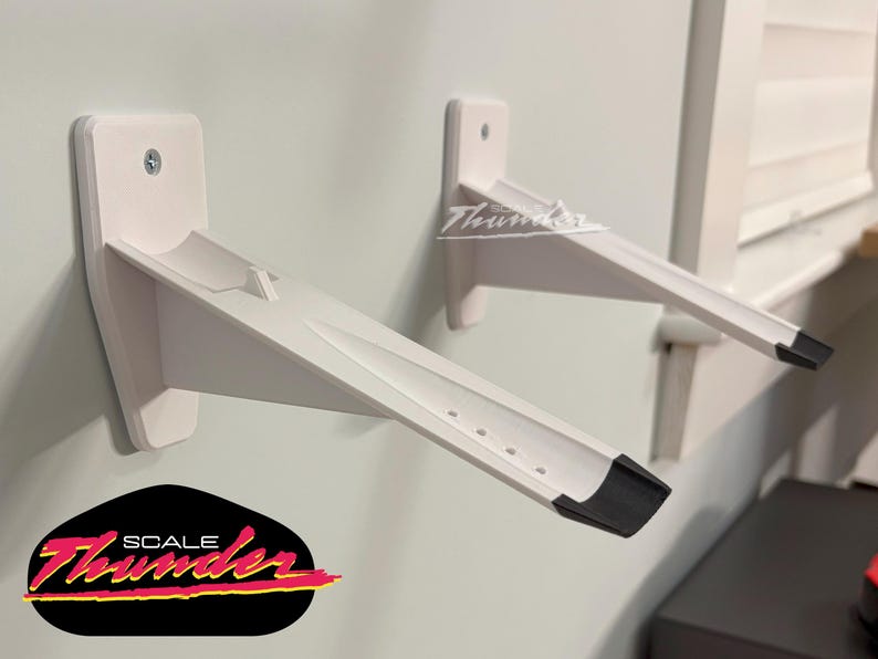May include: Two white wall-mounted shelf brackets with a black accent on the end. The brackets are mounted on a light gray wall. The logo "SCALE Thunder" is visible in the lower left corner.