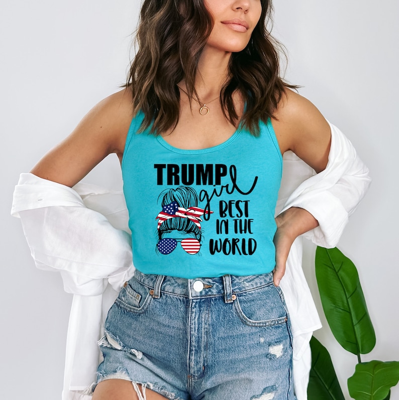 May include: A turquoise tank top with a graphic of a woman with a bun in her hair wearing sunglasses and a red, white, and blue headband. The text "Trump girl best in the world" is printed on the tank top.