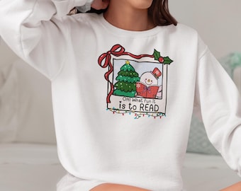May include: White sweatshirt featuring a framed graphic with a Christmas tree and a snowman reading a book. The graphic includes the text "OH! What fun it is to READ" in a playful font, with a red bow and holly accents.