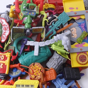 May include: A collection of Teenage Mutant Ninja Turtles toys, including figures, weapons, and accessories. The toys are made of plastic and feature bright colors, such as red, green, yellow, and blue. The toys are in good condition and appear to be from the 1990s.