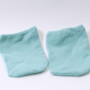 Puede incluir: Dos pares de calcetines de malla verde azulado claro se muestran sobre un fondo blanco. Los calcetines tienen un aspecto suave y texturizado y un efecto degradado, pasando de un verde azulado más oscuro en la parte superior a un tono más claro en la parte inferior.