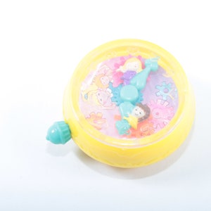 May include: A yellow plastic toy with a clear plastic face. The face has a colorful design with gears and cartoon characters. The toy has a blue plastic handle.