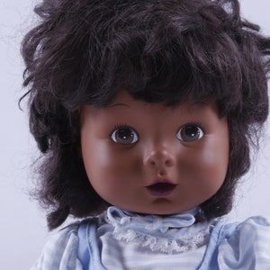 May include: A doll with dark brown curly hair, brown eyes, and a light blue and white striped dress. The doll has a light brown complexion.