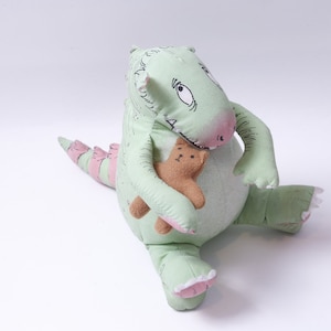 May include: A light green stuffed dinosaur toy with a pink snout, claws, and stripes on its tail. The dinosaur is holding a small brown teddy bear. The toy is made of soft fabric and has a whimsical design.