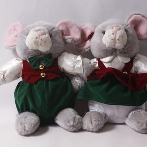 May include: Two plush grey mice with pink inner ears, wearing matching outfits. The left mouse wears a white shirt, dark red waistcoat with gold buttons, and green trousers. The right mouse wears a white shirt, dark red pinafore, and white trousers.