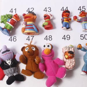 May include: A collection of Sesame Street character figurines and plush toys. The toys include Elmo, Ernie, Bert, Cookie Monster, and others. The figurines are made of plastic and the plush toys are made of fabric. The toys are numbered 41-50.