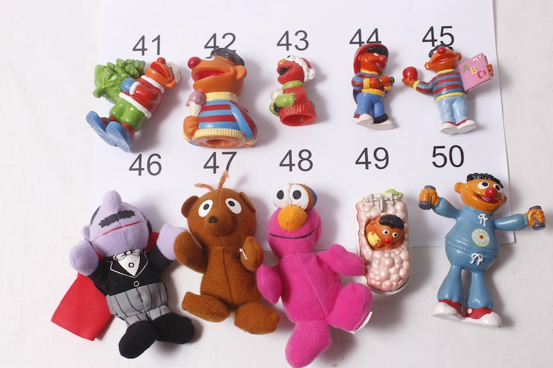 May include: A collection of Sesame Street character figurines and plush toys. The toys include Elmo, Ernie, Bert, Cookie Monster, and others. The figurines are made of plastic and the plush toys are made of fabric. The toys are numbered 41-50.