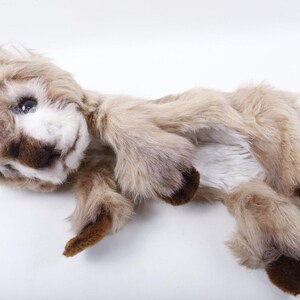May include: A plush, handmade stuffed animal in the shape of a fawn. The toy has a light brown and white fur with darker brown accents on the ears, feet, and face. The fawn has blue eyes and is lying down.