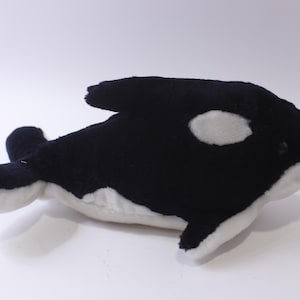 May include: Black and white plush orca whale toy. The orca has a white patch around its eye and a white belly.