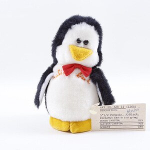 May include: A plush penguin toy with a black and white body, yellow beak, and red bow tie. The penguin is approximately 5.5 inches tall. A tag is attached with the text "ART NO. XJK 14 (1268)" and other details.