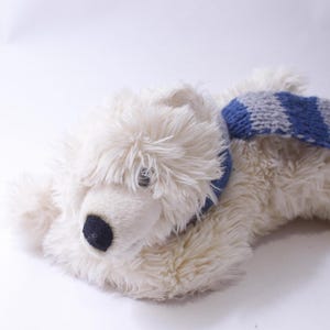 May include: A plush polar bear toy with white synthetic fur, a black nose, and dark eyes. The stuffed animal is wearing a knitted scarf featuring horizontal stripes in alternating shades of blue and grey, complete with fringe at the ends.