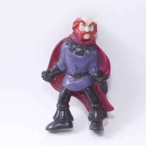 May include: A plastic toy figure of a man with a red beard and a purple tunic. He is wearing a red cape and black boots.