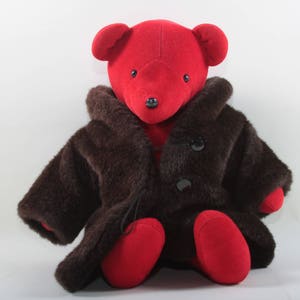 May include: A red teddy bear wearing a brown faux fur coat. The bear has black button eyes and a black nose.