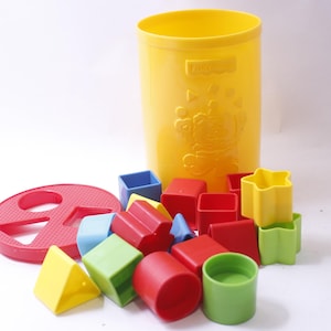 May include: A yellow plastic container with a lid and a set of colorful plastic shape blocks. The blocks include squares, triangles, stars, and circles. The container has the word "Learning" printed on it.
