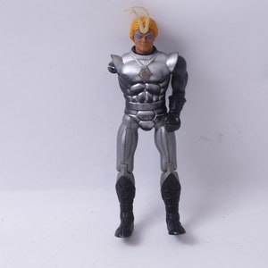 May include: A silver action figure with a black and silver suit, a yellow mohawk, and blue eyes. The figure is holding a silver weapon in its right hand.