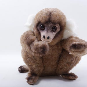 May include: A plush monkey toy in a seated position, featuring brown fur and a white collar. The monkey has a light-colored face with dark eyes and a small nose. The toy is set against a plain white background.