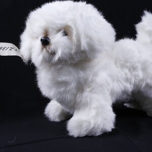 May include: A white plush toy dog with a tag that says "36/8-2". The dog is standing on a black surface.