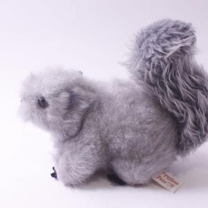 May include: A plush gray squirrel toy with a fluffy tail. The stuffed animal has small black eyes and a tag that reads "Pillow Pets". The toy is made of soft, fuzzy material.