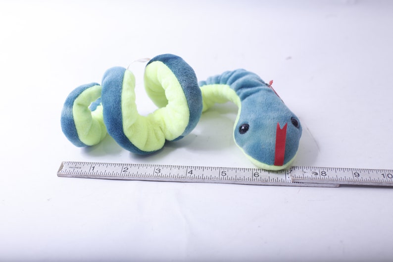 Pode incluir: Um brinquedo de cobra de pel&uacute;cia azul e verde com uma boca vermelha. A cobra est&aacute; enrolada e mede cerca de 15 cm de comprimento.