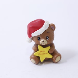 May include: A brown teddy bear wearing a red Santa hat holds a yellow star that says "Beary Christmas".