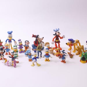 Könnte beinhalten: Eine Sammlung farbenfroher Disney-Charakterfiguren, darunter Donald Duck, Mickey Mouse, Goofy und Pluto. Die Figuren sind in verschiedenen Posen und Outfits vor einem weißen Hintergrund. Es gibt eine Vielzahl von Größen und Stilen.