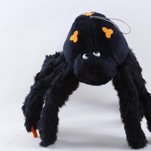 Puede incluir: Un juguete de peluche de araña negra con detalles en naranja. La araña tiene patas largas y esponjosas y un cuerpo redondo con marcas naranjas. Tiene ojos blancos y un lazo de metal para colgar. Una divertida decoración de Halloween.