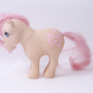 May include: A pink My Little Pony toy with a pink mane and tail. The pony has a pink heart pattern on its flank.