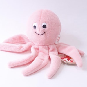 May include: Pink plush octopus with a smiling face and large eyes. The octopus has eight tentacles and is wearing a red Ty tag.