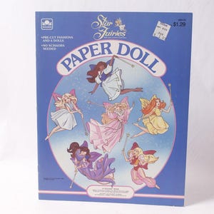 May include: A vintage "Star Fairies Paper Doll" set. The cover is blue with illustrations of fairies in various outfits. Text includes "Pre-cut fashions and 6 dolls. No scissors needed."