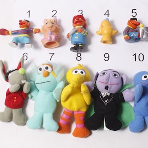 May include: A collection of ten Sesame Street character figurines and plush toys. The toys include Elmo, Big Bird, Cookie Monster, and others. The toys are in various colors, including red, blue, yellow, and purple. The toys are numbered 1 through 10.