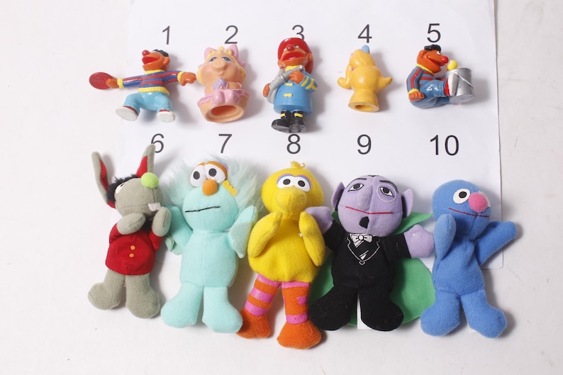 May include: A collection of ten Sesame Street character figurines and plush toys. The toys include Elmo, Big Bird, Cookie Monster, and others. The toys are in various colors, including red, blue, yellow, and purple. The toys are numbered 1 through 10.