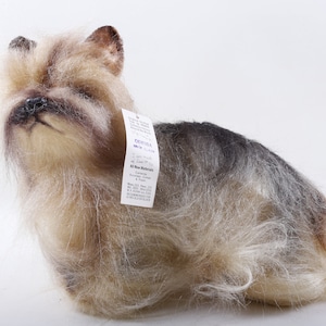 May include: A plush Yorkshire Terrier dog figurine with a realistic appearance. The dog has a mix of tan, gray, and black fur. A tag is attached to the dog's ear. The dog is posed in a sitting position.