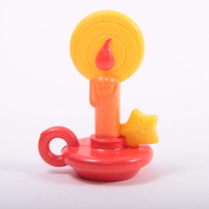 May include: A red and yellow plastic candle with a star-shaped handle. The candle has a yellow flame and a red base.