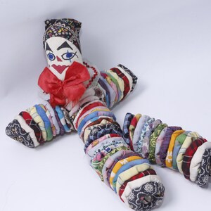 May include: A colorful rag doll with a painted face, red bow, and a black and white patterned hat. The doll is made of fabric scraps sewn together in a circular pattern.