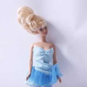 May include: A blonde doll wearing a light blue strapless dress with a tulle skirt. The doll has a high bouffant hairstyle.