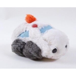 May include: A plush toy shaped like a vehicle with white faux fur, dark gray wheels, and light blue accents. It features a small orange pom-pom on top, a red circular detail, and two black plastic eyes on the front side of the soft stuffed body.