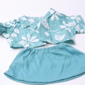 May include: A turquoise and white floral print shirt and matching turquoise skirt set. The short-sleeved shirt has a collared neckline. The skirt has an elastic waistband. The set is made of a soft, lightweight fabric.