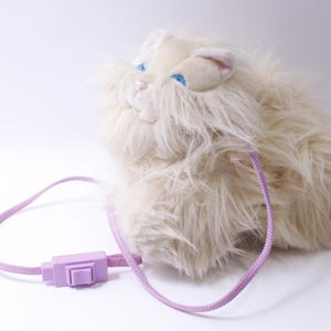 May include: A white plush cat toy with blue eyes and a pink cord attached to a purple switch.