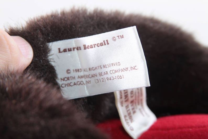 May include: A white tag with brown text that reads "Lauren Bearcall TM 1983 All Rights Reserved North American Bear Company, Inc. Chicago, NY (312) 943-4061".