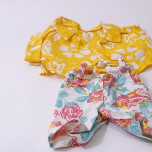 May include: A yellow collared shirt and matching shorts set. The shirt is yellow with white floral patterns. The shorts are white with pink, blue, and yellow floral patterns. The set is made of a lightweight fabric.