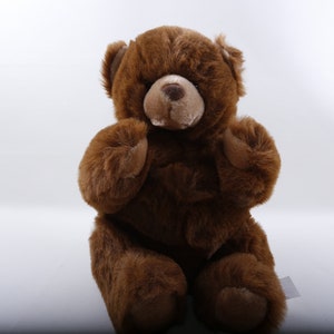 May include: A brown teddy bear with a soft, plush fur. The bear is sitting with its paws in front of it and has a sweet, innocent expression.