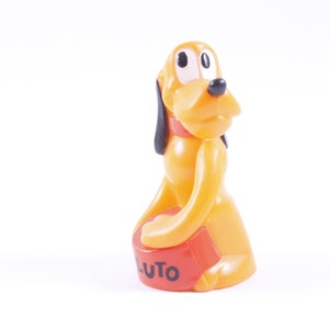 Peut inclure: Un jouet en plastique jaune de Pluto, un chien de dessin animé de Disney, assis avec ses pattes avant sur un bol en plastique rouge qui dit "Pluto" en lettres noires.