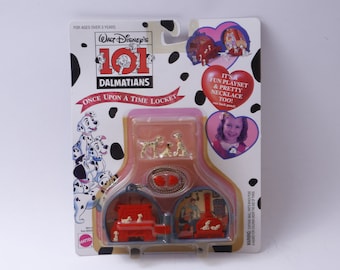 Può includere: Una confezione di plastica con sfondo rosa e bordo bianco. La confezione contiene una collana 101 Dalmatiani Once Upon a Time Locket. Il ciondolo è aperto e mostra una scena del film. La confezione include anche una piccola figurina di un dalmata. Il testo sulla confezione recita "Walt Disney's 101 Dalmatiani Once Upon a Time Locket".